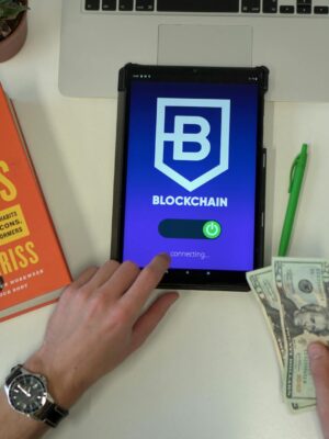 Flat lay image featuring a tablet with blockchain app, US dollars, and a book on a desk.