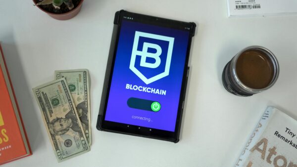 Tablet displaying a blockchain app interface with US dollars, books, and coffee on a white table.